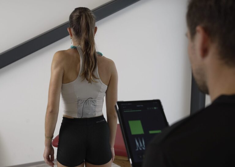 Sportlerin ist mit Elektroden ausgestattet und führt Übungen aus. Der Physiotherapeut sitzt mit Tablet und Myoact Software Biofeedback. female Athlete coach physiotherapist