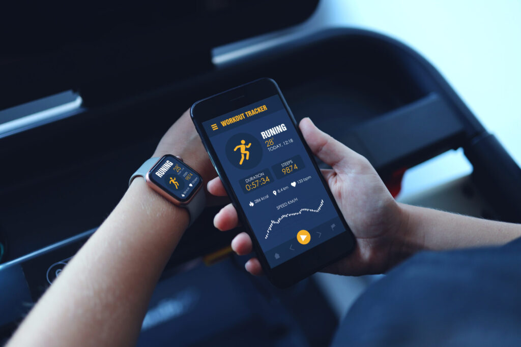 Sportlerin benutzt Smartphone und Smartwatch auf dem Laufband und erfaast Leistungsparameter um ihre Leistungsfähigkeit zu bestimmen